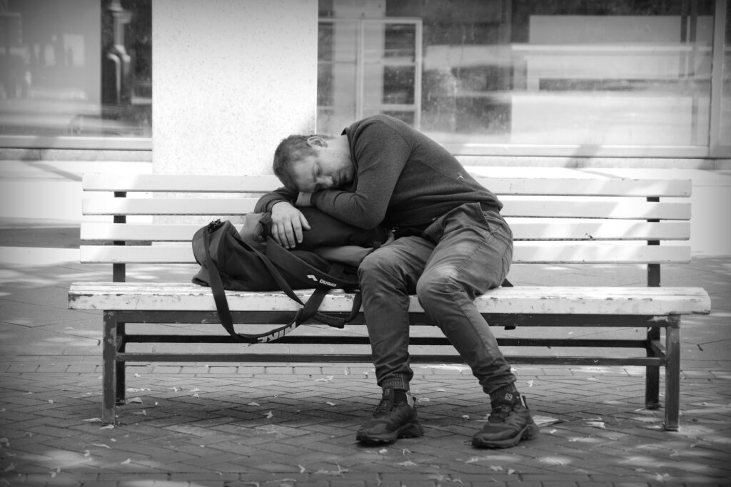 A man sleeping across his rucksack on one of the few available benches in the centre of the shopping area in Hannover.