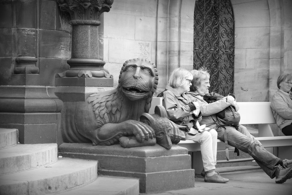 Mythical lion cradling a goat between its paws in front of the Dom in Bremen. Two tourists sitting behind looking in the other direction.