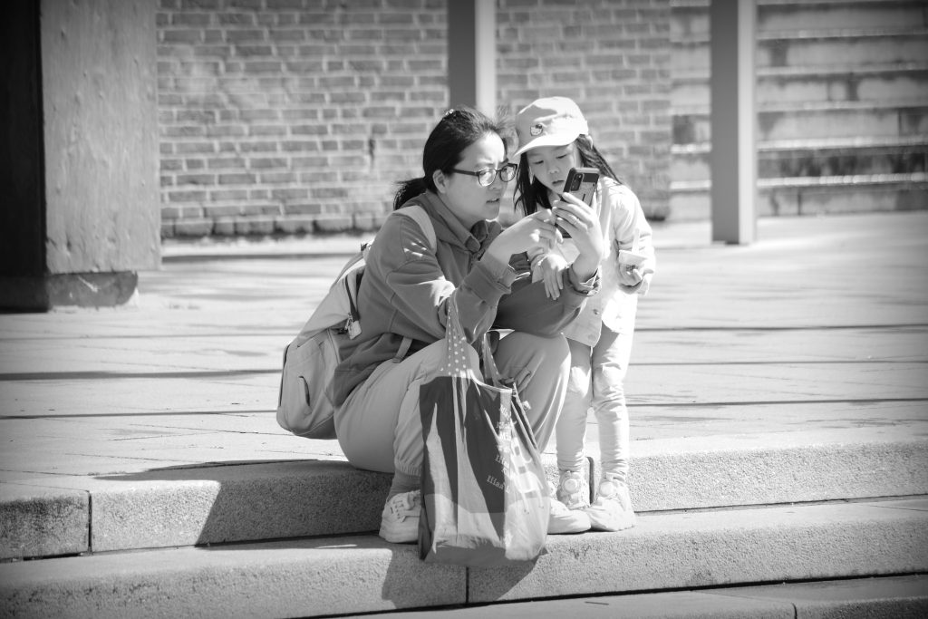 Asian mother and daughter sitting on steps in the Marktplatz in Bremen. The mother has a mobile, the daughter is looking over her shoulder.