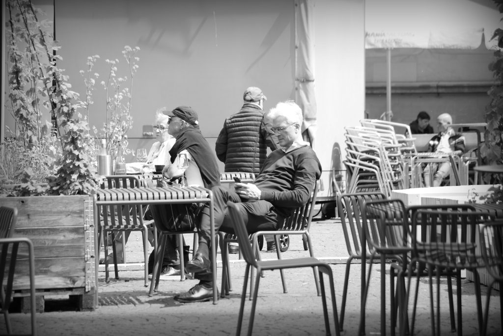 A man sitting at an outside restaurant table on Marktplatz, Bremen, checking his mobile.