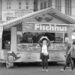 A fish stand called Fischhus in the Marktplatz, Bremen, with several people standing around looking up toward the sky where trapeze artists are performing.