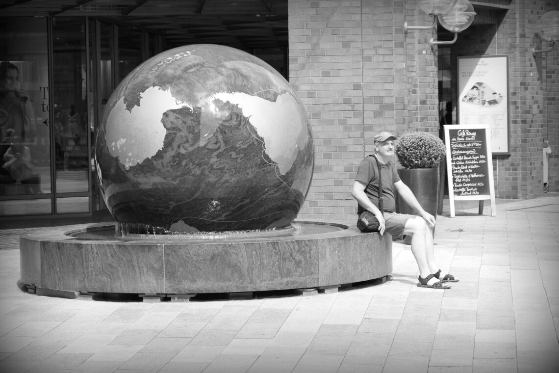 A lone man sitting in front of a massive stone globe, set up as a fountain, in Hamburg.