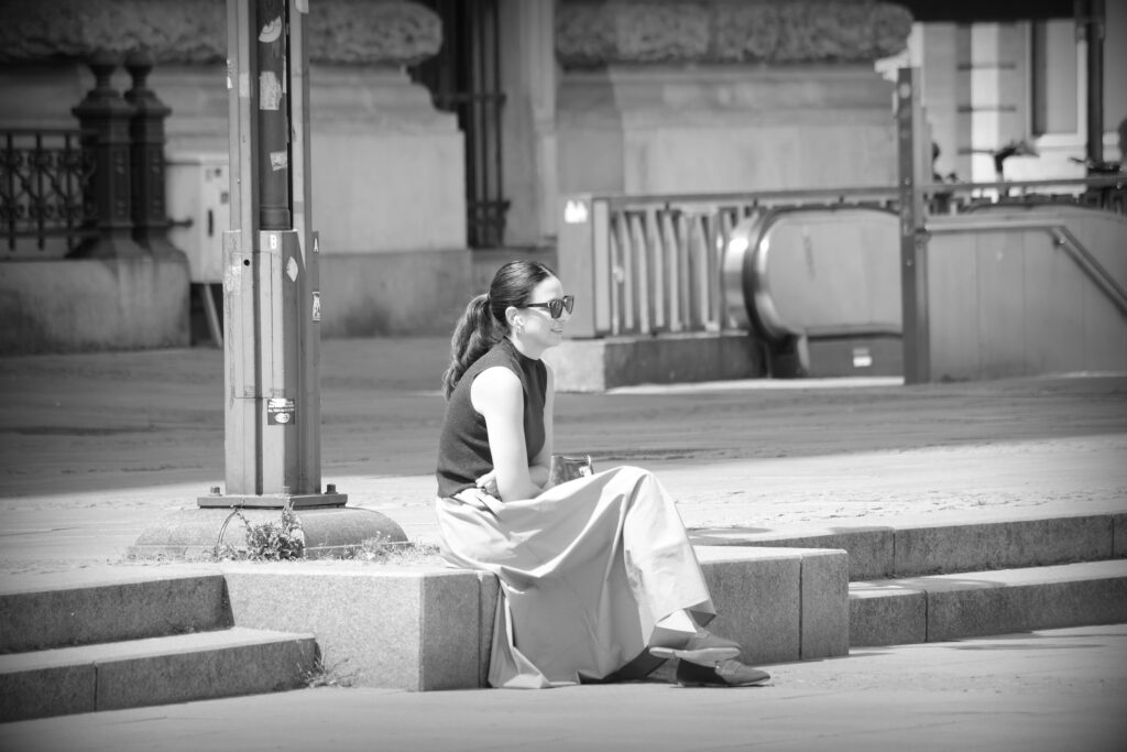 A single woman with dark glasses sitting on a stone step in the centre of Hamburg.
