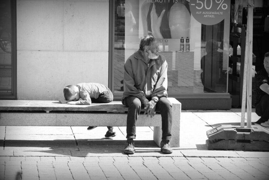 Homeless man in Osnabrück close to a tired child lying on a concrete bench.
