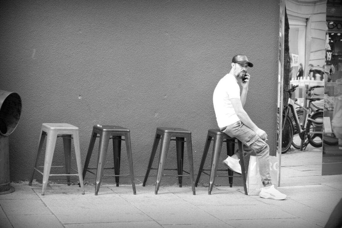 A bearded man sitting on one of a line of plastic stools next to a mirror in Osnabrück.