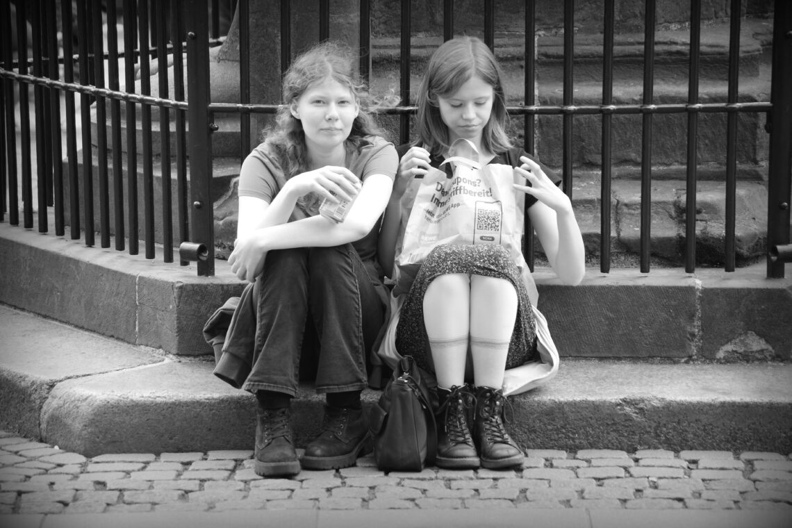 Two young women sitting together on the stone steps under the Roland statue in Bremen.