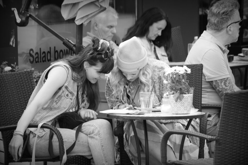 Two women at a coffee house table leaning over a smartphone.