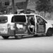 A taxi driver in shorts, sitting with his feet hanging out of the back passenger door of his vehicle in Hildesheim.