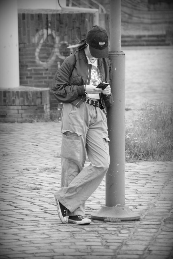 A young woman leaning against a streetlamp with her mobile in Bremerhaven.