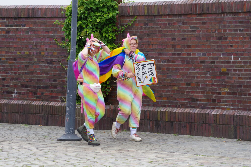 Two multi-coloured unicorns - with a sign offering Free Hugs and Free Pictures - at CSD Bremerhaven.