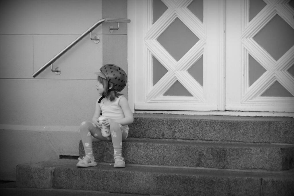 A small child wearing a bicycle helmet, holding a water bottle, sitting on stone steps in Schwerin.