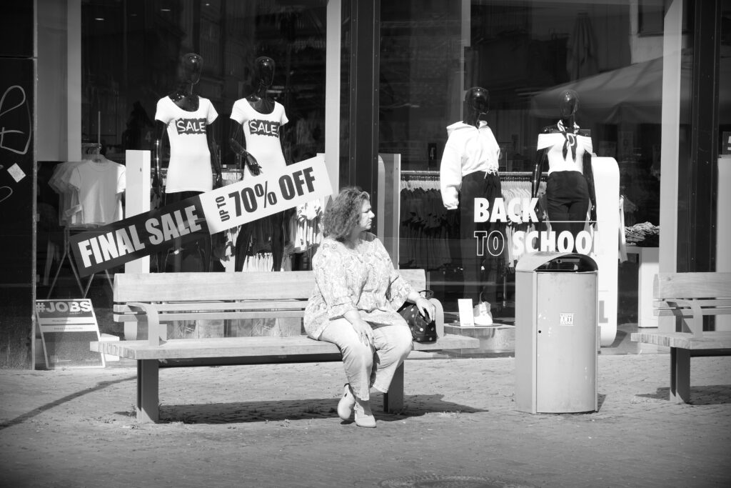 A woman sitting on a street bench in front of Back to School and Sale adverts in a shop window in Braunschweig.