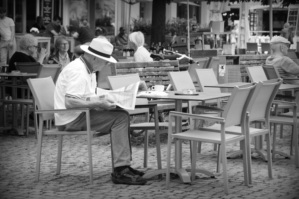 A man wearing a broad-rimmed hat reading a newspaper at an outside café in Braunschweig.