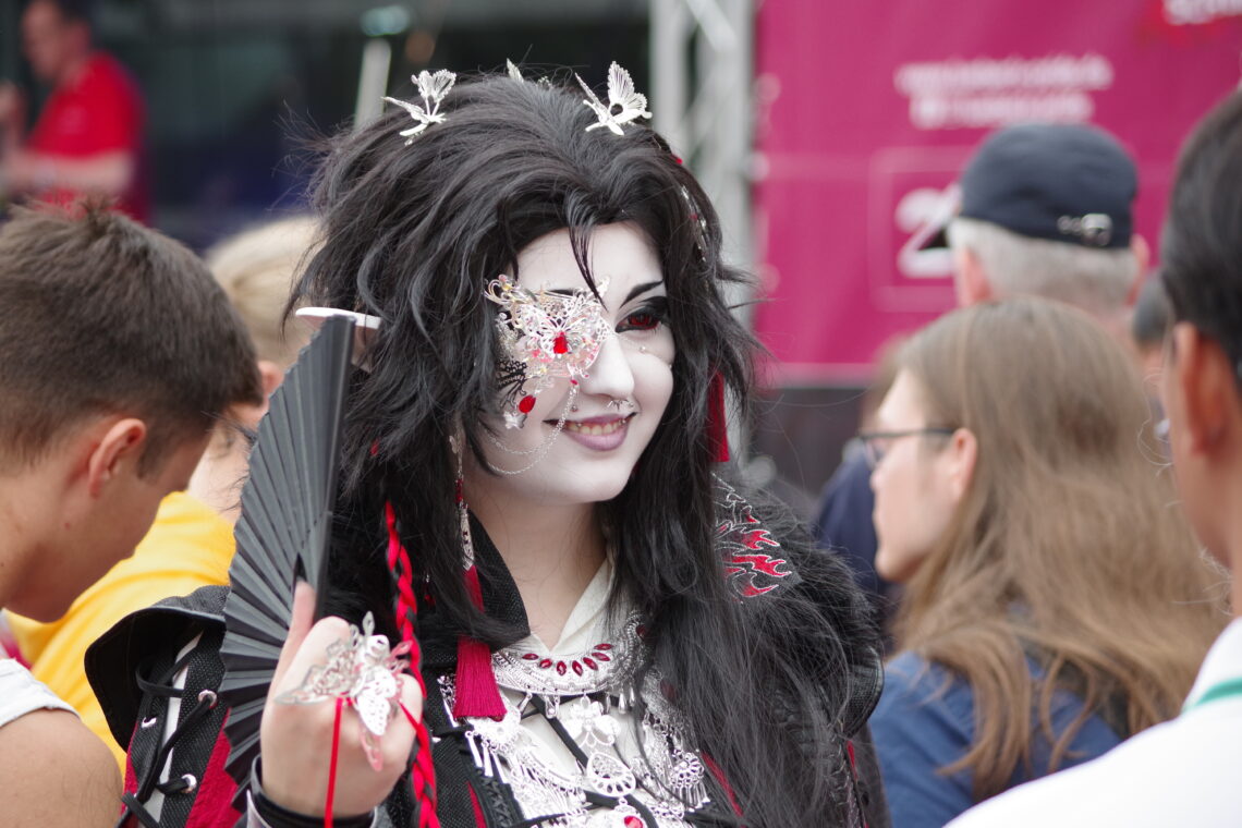 CSD Lübeck: a young person dressed in a stunning black and scarlet dress - very Japanese anime - with silver jewelry, a silver eye-pad, and carefully made up without going over the top.