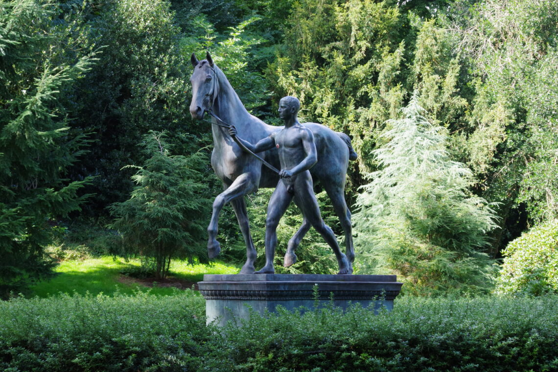 A statue from the centre of Bremen, Germany, with a naked man leading a horse, surrounded by trees.