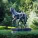 A statue from the centre of Bremen, Germany, with a naked man leading a horse, surrounded by trees.