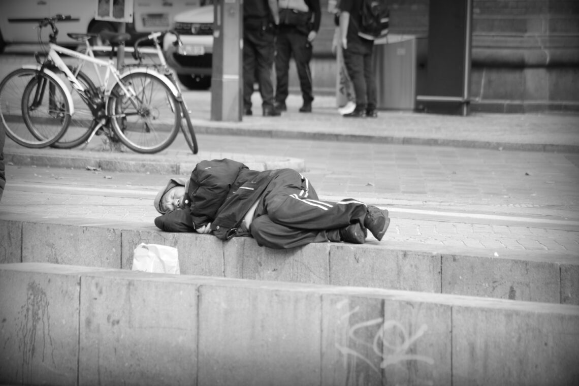 Black and white photograph of a man lying on a concrete wall , wrapped up against the cold, close to the main railway station in Bremen, Germany.