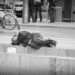 Black and white photograph of a man lying on a concrete wall , wrapped up against the cold, close to the main railway station in Bremen, Germany.