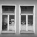 A black and white photograph of two double wood-frame windows, partially covered with white paint advertising a former textile handler. From a side street in Würzburg, Germany.