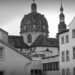 A black and white view of a religious building seen between the walls and roofs of other buildings in Würzburg.