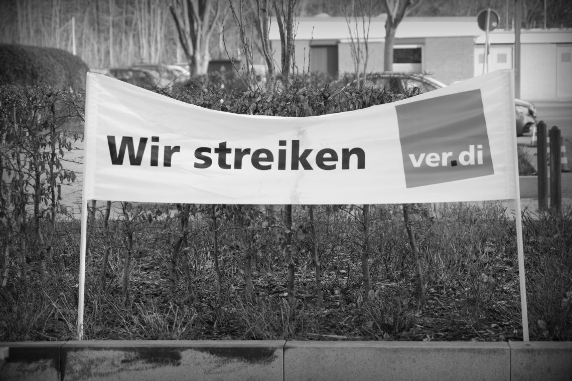 Black and white photograph of a protest banner with the words "Wir streiken" (We're striking) and the name of the union.