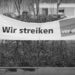 Black and white photograph of a protest banner with the words "Wir streiken" (We're striking) and the name of the union.