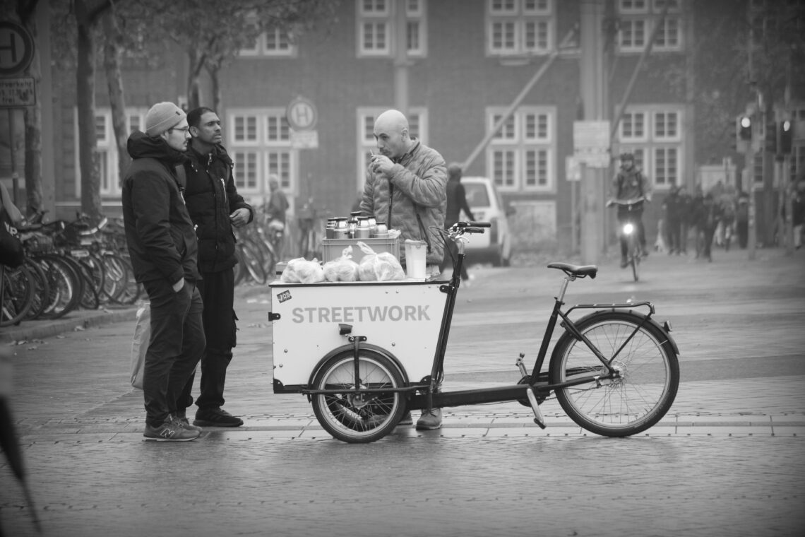 Black and white photograph of a group serving coffee to homeless people at Bremen railway station. Copyright Urban Camera.
