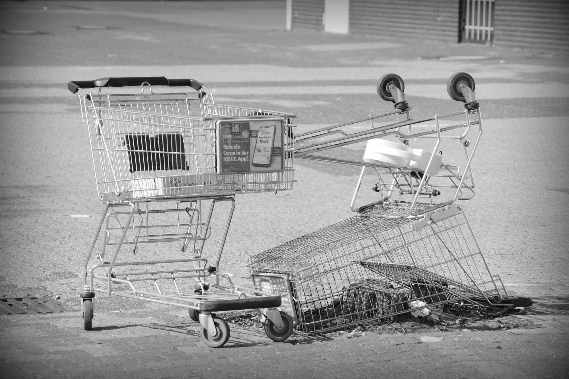 A monochrome photograph of two metal shopping trolleys, one upside down, abandoned in a deserted paved car park in Hemelingen, Bremen. Copyright Urban Camera.