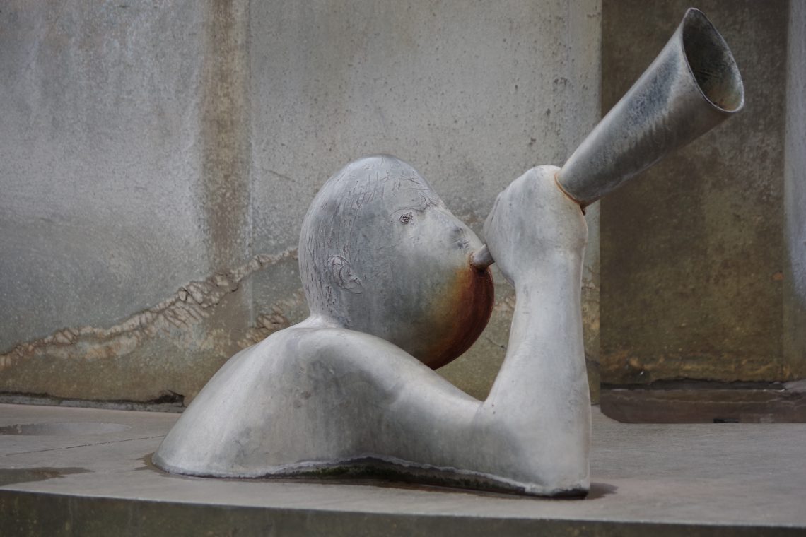 A natural coloured photograph of a metal statue, an indiscriminate upper-body figure blowing a trumpet. Copyright Urban Camera.
