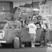 A monochrome photograph of a mobile coffee shop built into a VW traveller. The side of the VW opens upwards and customers are standing ordering drinks. Copyright Urban Camera.