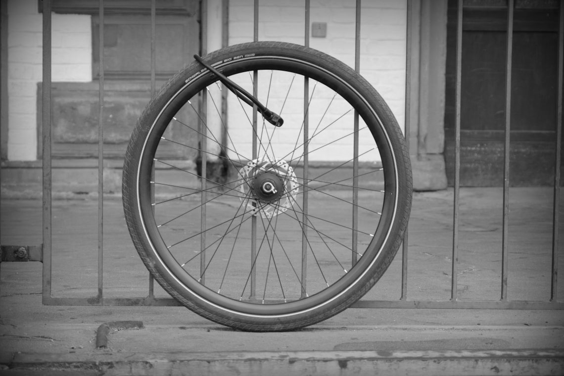 Monochrome photograph of a single bicycle wheel locked to railings outside the railway station in Düren, Germany. Copyright Urban Camera.