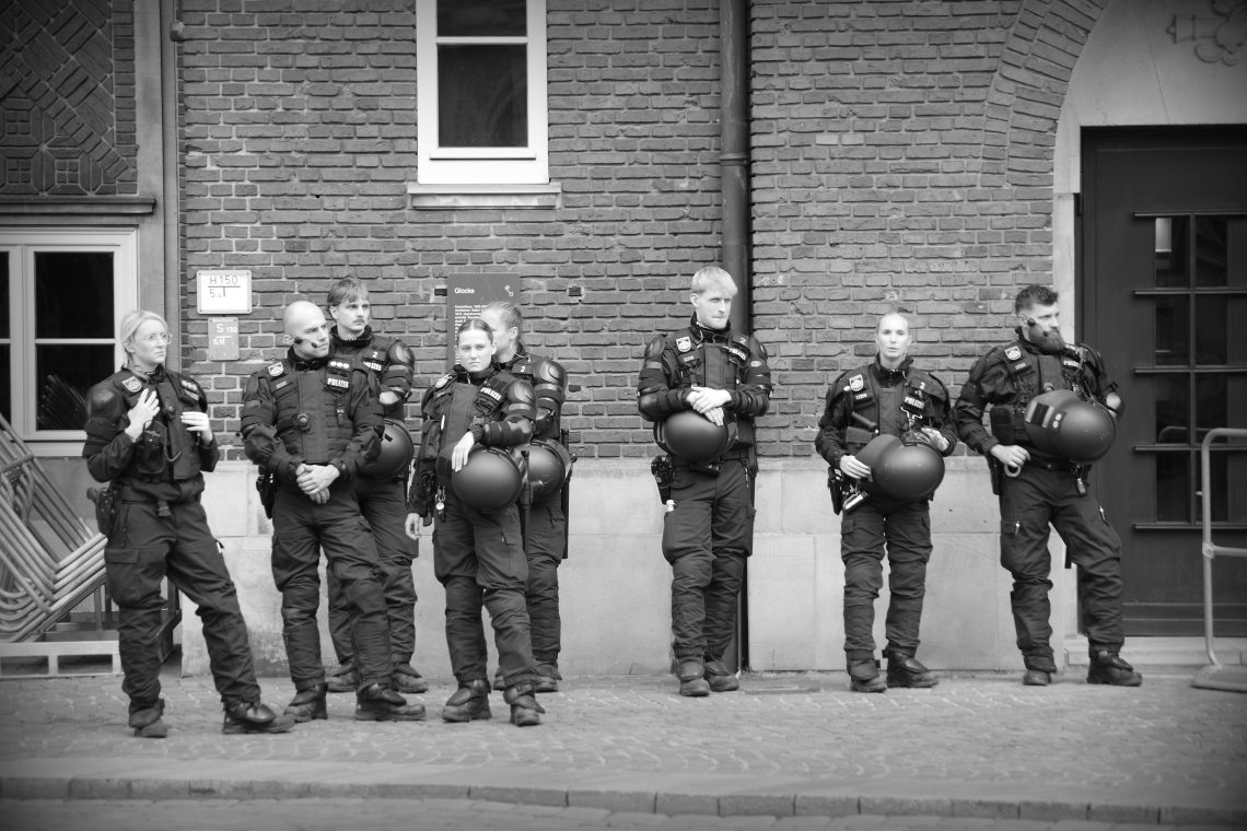 Monochrome photograph of a line of police officers in Bremen, Germany, attending an AfD publicity stunt, all dressed up with riot gear available. Copyright Urban Camera.